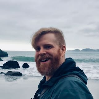 Average height, pale skin, red hair and beard, at a beach on a gloomy day with camera.